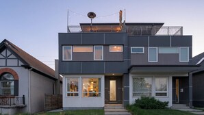 A modern two-story house with a balcony, large windows, and a visible interior with a ceiling fan.