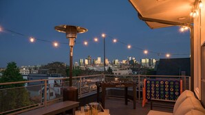 A rooftop terrace with a city skyline view, string lights, a table with drinks, and a sofa.