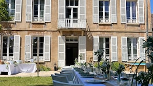 Ein großes Gebäude mit einer symmetrischen Fassade, zahlreichen Fenstern mit Fensterläden und einem zentralen Eingang.