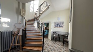 Eine Wendeltreppe mit Holzhinweisstufen und schwarzen Geländern, die zu einem Raum mit gemusterten Bodenfliesen und einem Bild von Hirschen an der Wand führt.