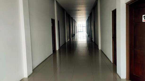 A long, narrow hallway with white walls and a tiled floor, leading to a door with a sign indicating a room number. - Nusantara Bypass Mojokerto By Reccoma (Mojokerto)