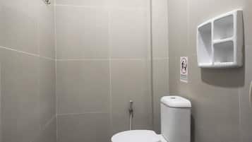 A small, modern bathroom with a white toilet, a hand dryer, and a no-smoking sign.