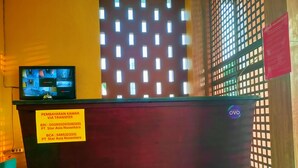 A reception desk with a monitor displaying security cameras, a sign with transfer information, and a wooden partition with a grid pattern. - Nusantara Bypass Mojokerto By Reccoma (Mojokerto)