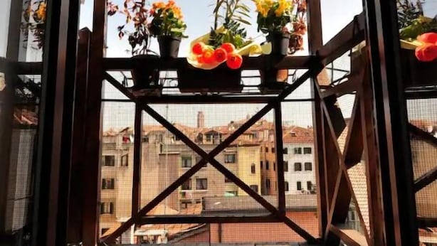 Un balcone in legno con ringhiera metallica, piante in vaso e vista su edifici sullo sfondo.