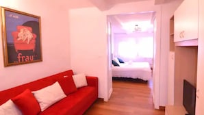 Una stanza con un divano rosso, un letto e una televisione.