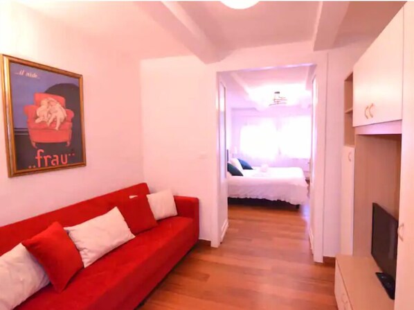 A room with a red sofa, a bed, and a TV.