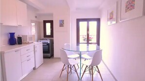 Una cucina moderna con mobili bianchi, un fornello e un tavolo da pranzo in vetro con quattro sedie.