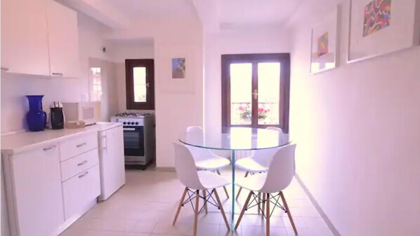 Una cocina moderna con armarios blancos, una estufa y una mesa de vidrio con cuatro sillas.
