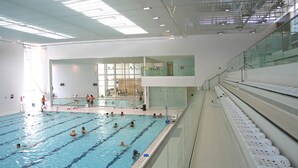 An indoor swimming pool with multiple lanes, a glass railing, and a staircase leading to a second level. - Luxury 2 Bed Designer Flat with Private Garden in London (Bexleyheath)