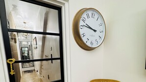 A room with a wooden herringbone floor, a brown leather chair, a large wall clock, and a black-framed door with a golden handle. - Luxury 2 Bed Designer Flat with Private Garden in London (Bexleyheath)