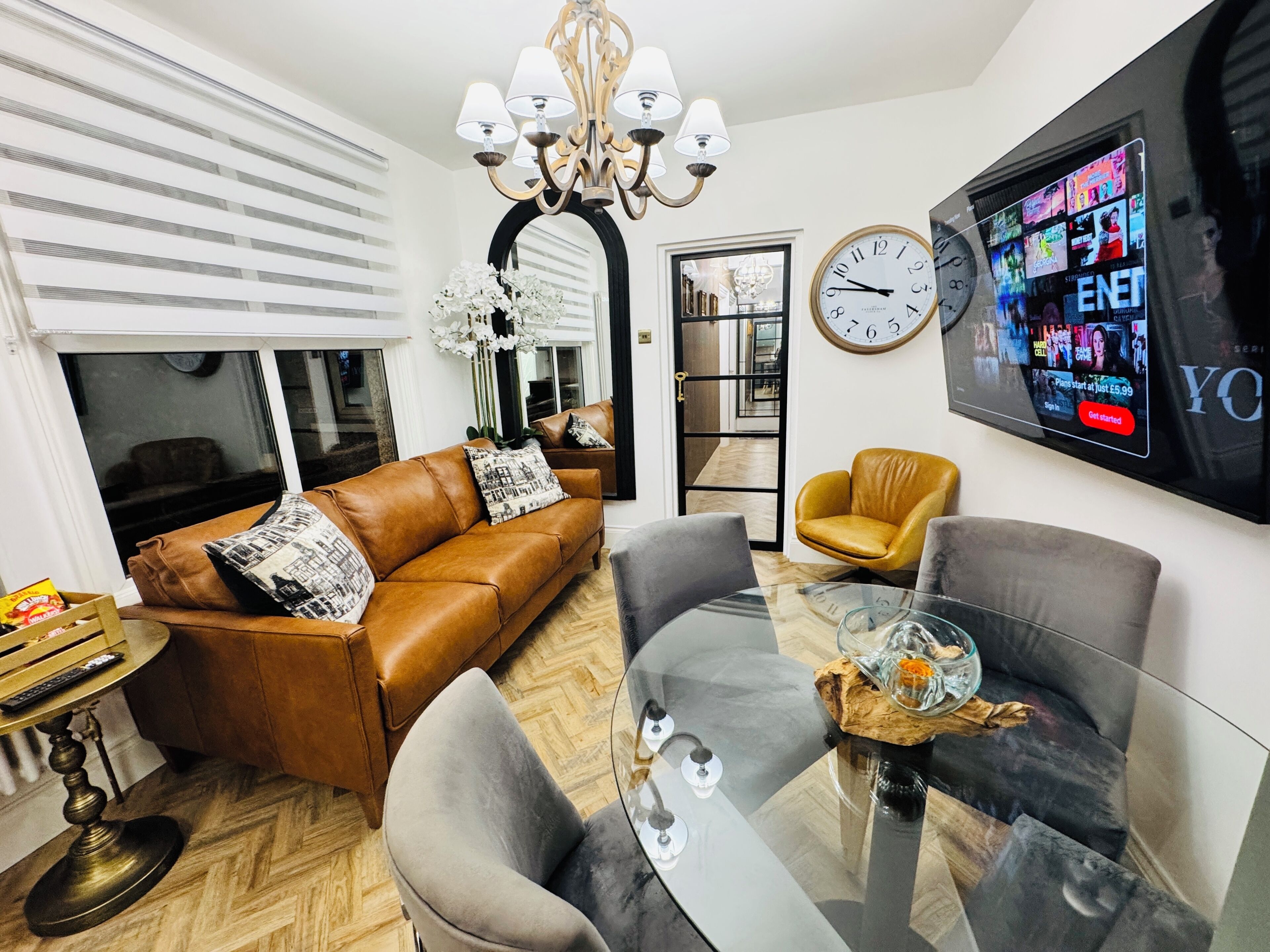 A modern living room with a brown leather sofa, a glass coffee table, and a television mounted on the wall displaying a movie.