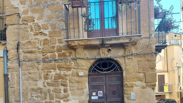 A stone building with a wooden door and a balcony with plants. - Gamez Floor Apartment 67 (Agrigento)