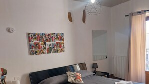 A hotel room with two beds, a wall-mounted comic book art piece, a hanging light fixture, and a window with curtains. - Gamez Floor Apartment 67 (Agrigento)