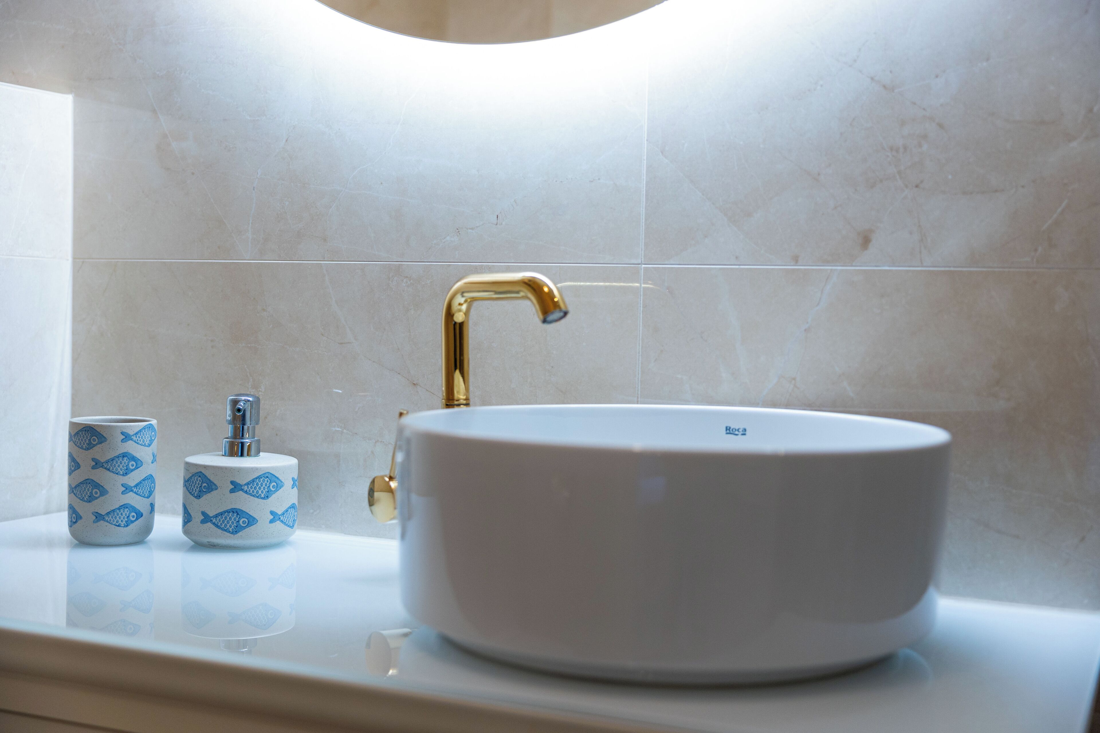 A bathroom with a white sink, gold faucet, and two fish-patterned soap dishes.