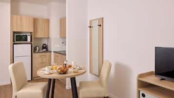 A compact living space with a kitchenette, a dining area with two chairs, a flat-screen TV, and a mirror.