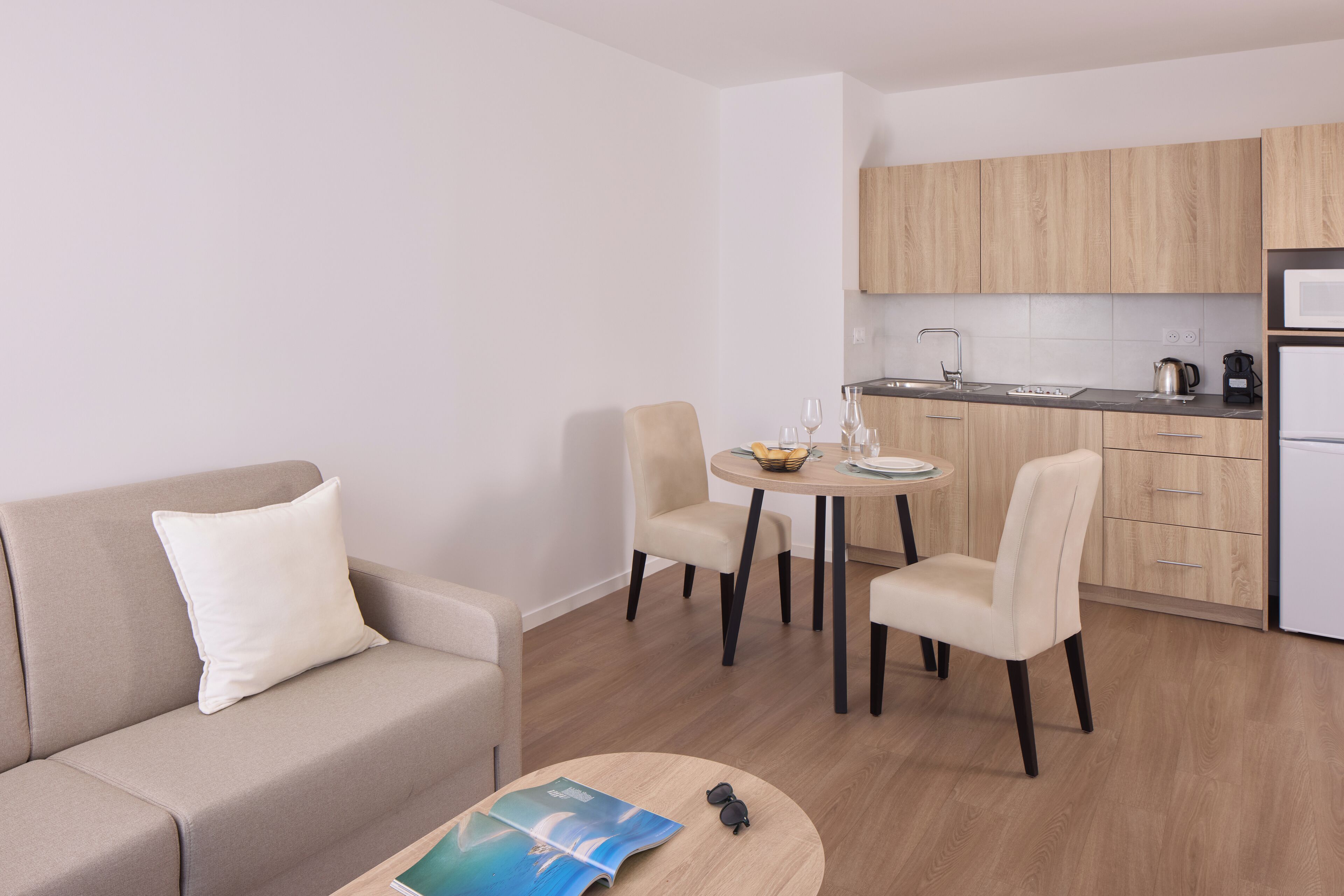 Una sala moderna con un sofá, una mesita redonda y una zona de comedor con dos sillas y una mesa pequeña.