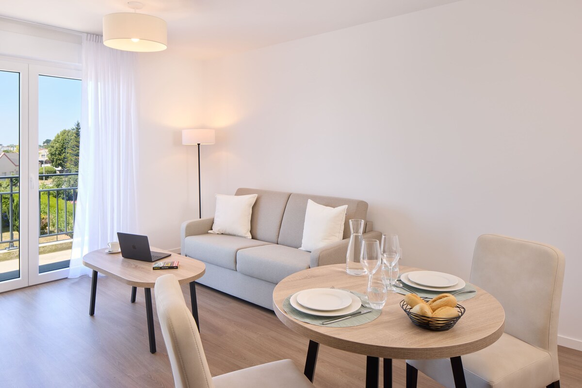 Een moderne woonkamer met een bank, een eettafel gedekt met borden en glazen, een laptop en een schaal met brood.