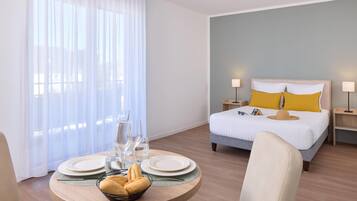 Une chambre d’hôtel avec un lit, des lampes de chevet, une table à manger avec des assiettes et des verres, et une fenêtre avec des rideaux.