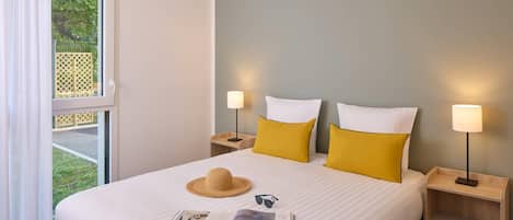 Una cama bien hecha con una revista, un sombrero de paja y dos lámparas en las mesitas de noche.
