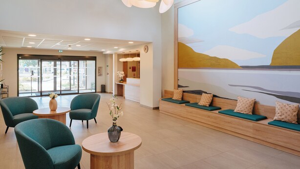 A spacious lobby with seating areas, a reception desk, and a large window providing a view of the outdoors.