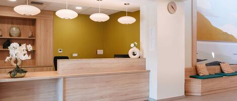 A reception area with a wooden reception desk, a clock on the wall, and a seating area with cushions.