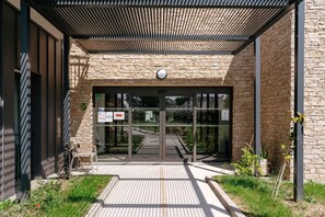 Une entrée moderne, avec une façade en pierre, des portes en verre et une structure de toit en métal.