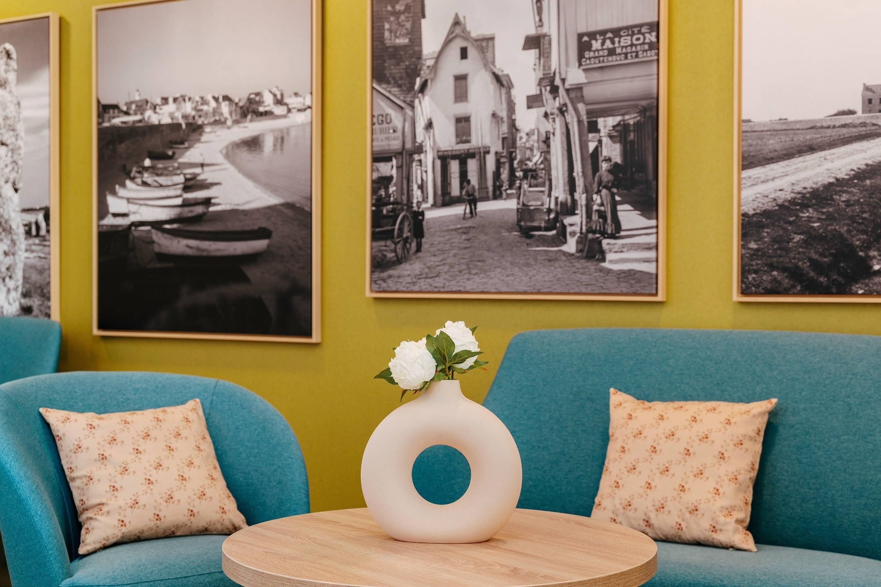 Una habitación con sofás color turquesa, una mesa redonda de madera y un jarrón blanco con flores.