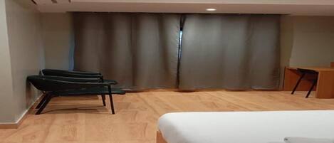 Una habitación de hotel con cama, una silla, un escritorio y una cortina.