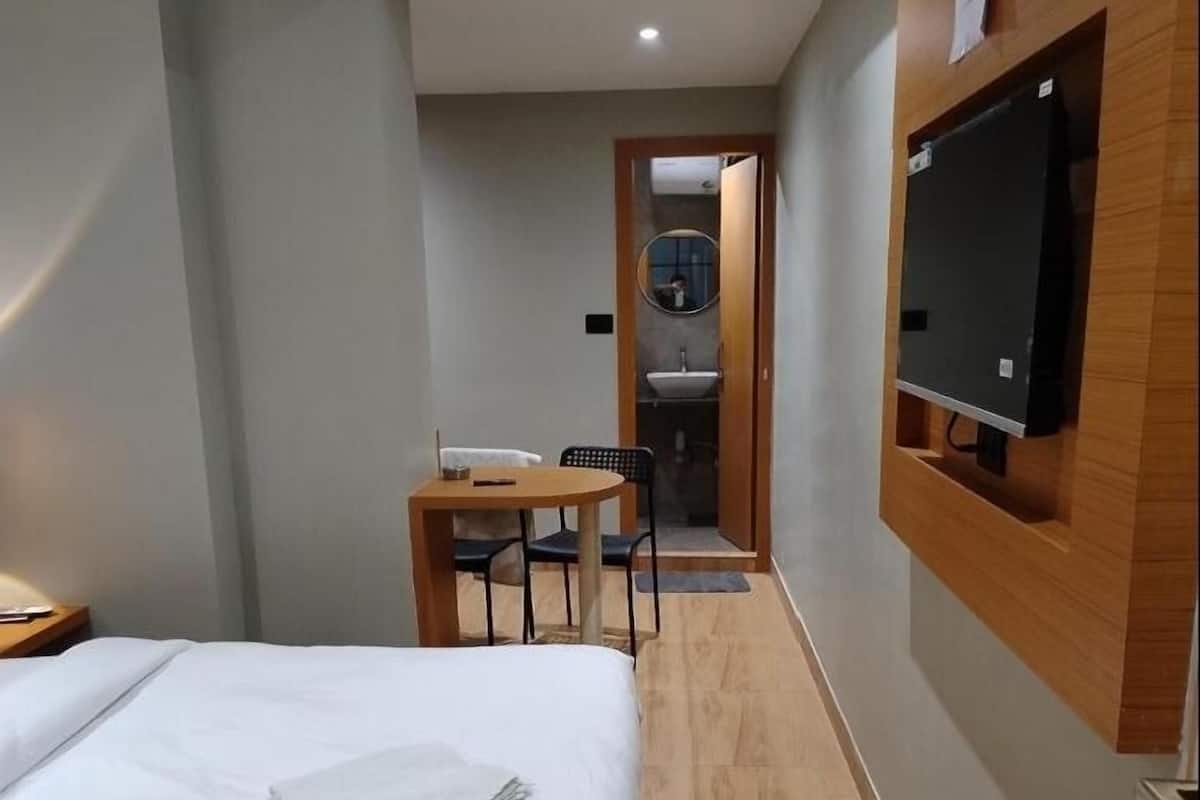 A modern bedroom with a bed, a wooden desk, and a small kitchenette area.
