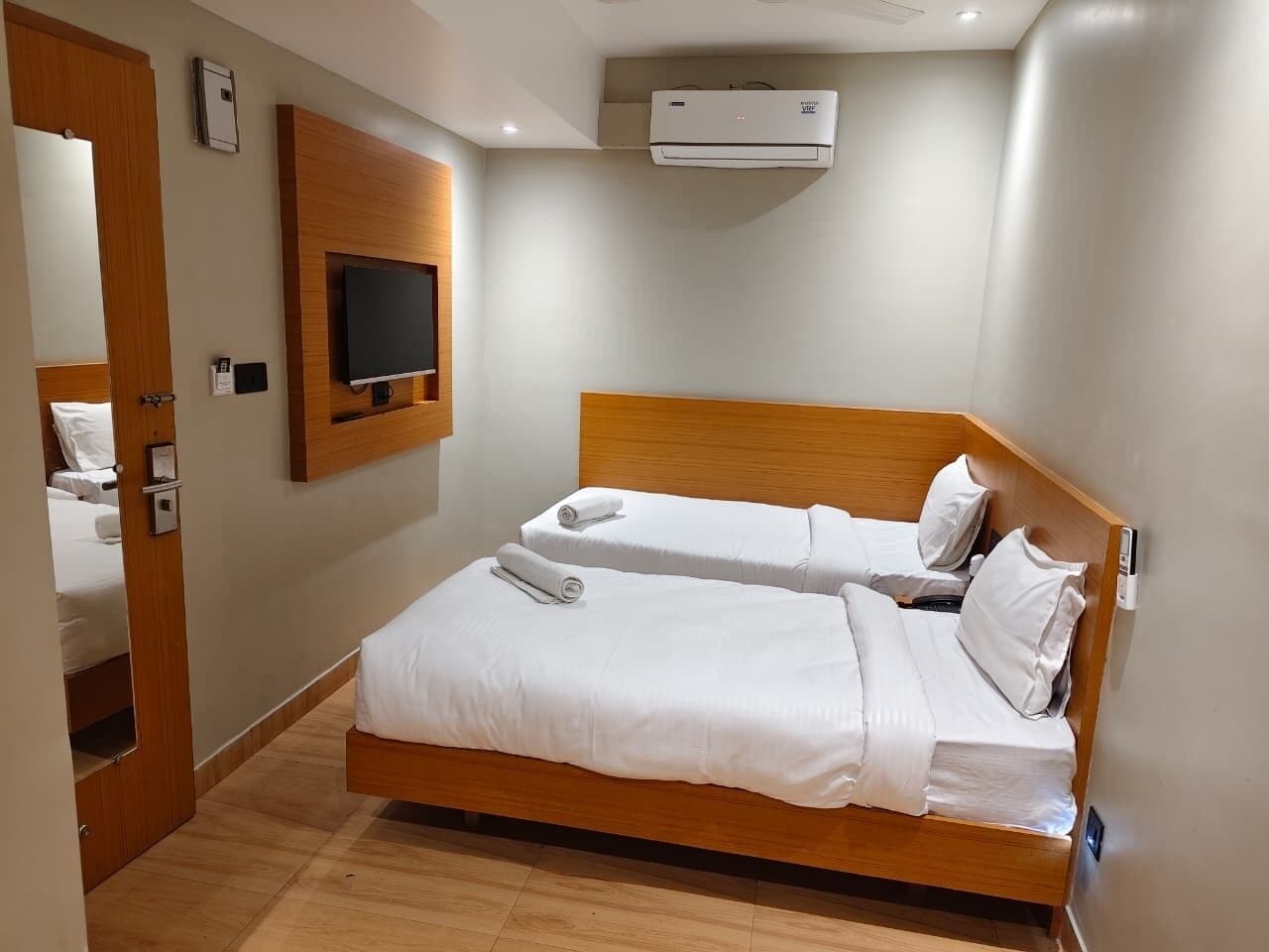 Una camera d'albergo con un letto in legno, una TV a schermo piatto montata a parete e un condizionatore d'aria sopra il letto.