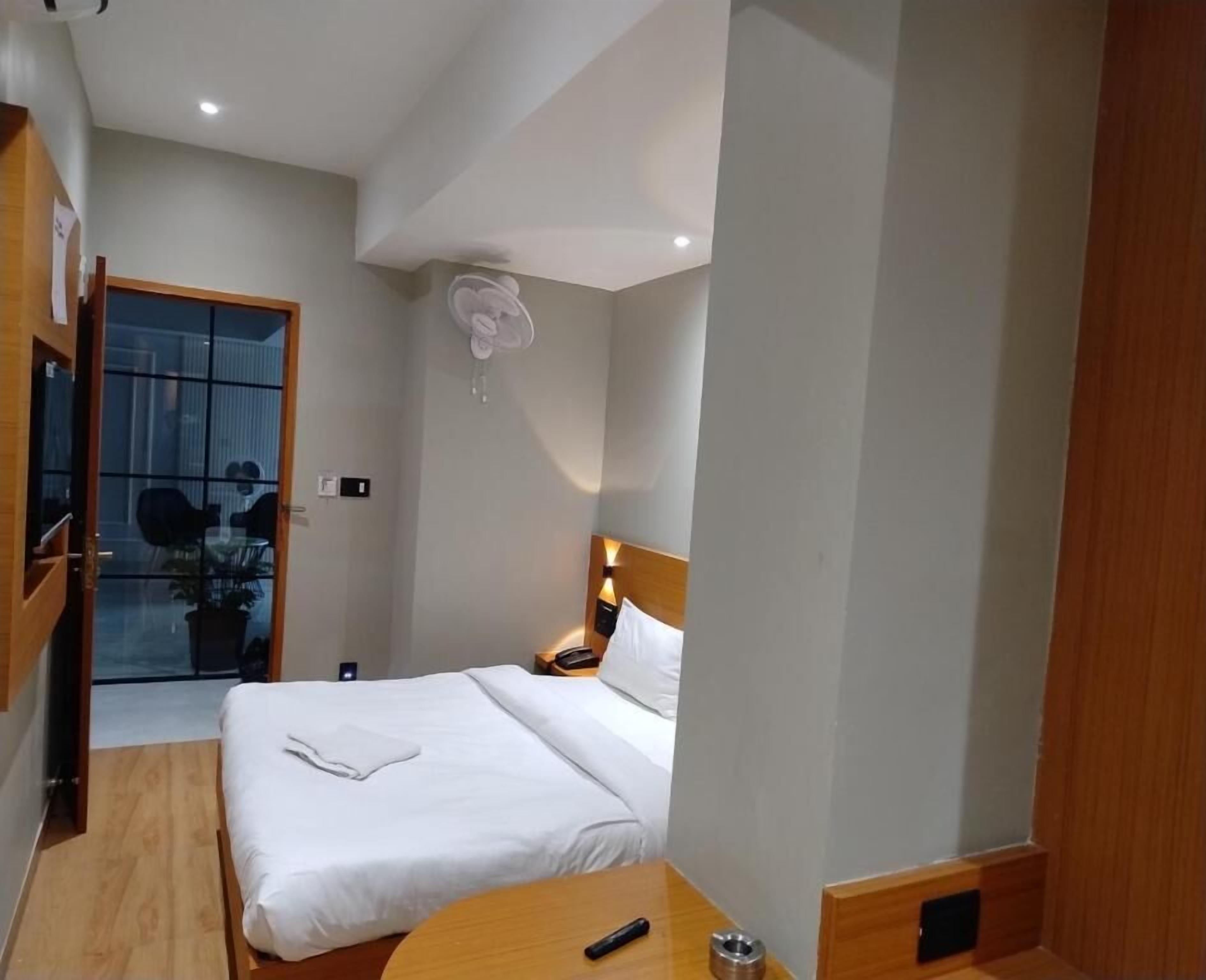 Et hotelværelse med seng, sengebord og et lille bord med fjernbetjening.
