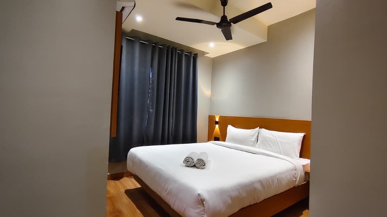 Una habitación de hotel con cama, ventilador de techo y ventana con cortinas.