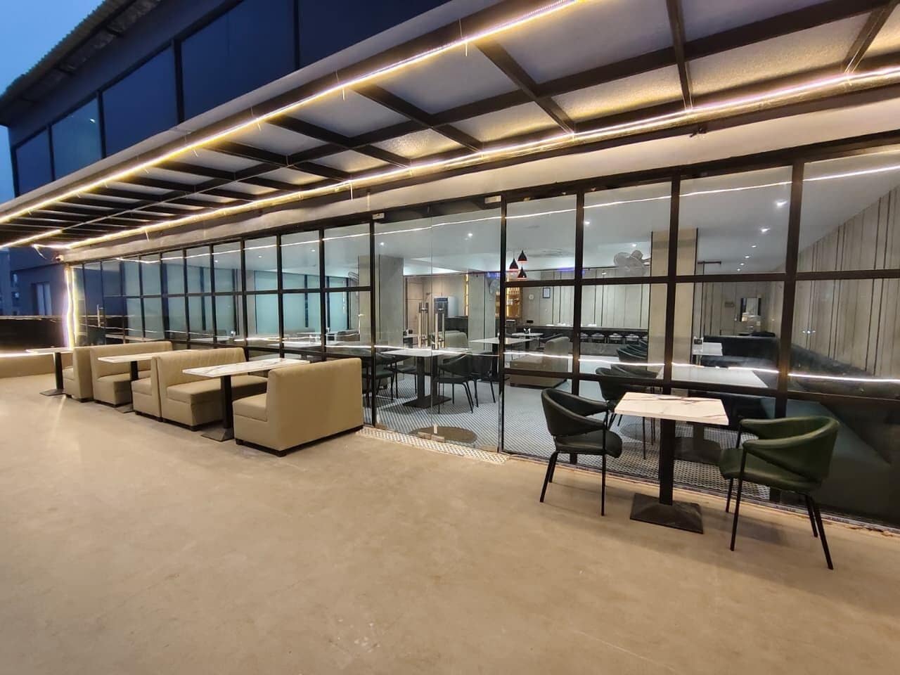 An outdoor seating area with tables and chairs, a glass wall, and a modern building in the background.