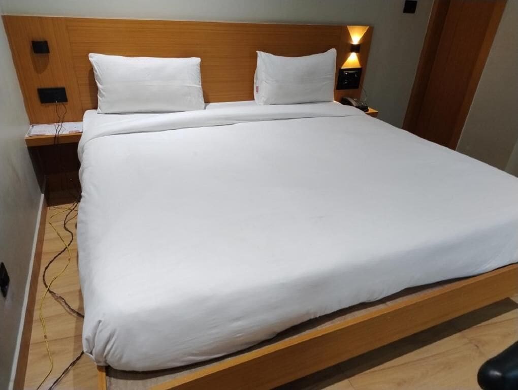A neatly made bed with white linens, a wooden headboard, and a bedside table with a lamp.