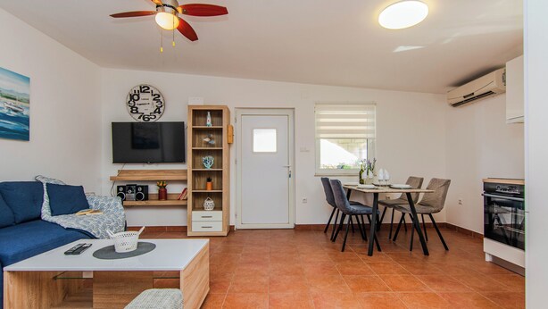 Un espace de vie compact comprenant un canapé, un téléviseur, un coin repas et une kitchenette.