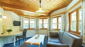 A cozy room with a wooden ceiling, a sofa, a table, a TV, and large windows with curtains. - Chalet Felix by we rent (Saalbach)