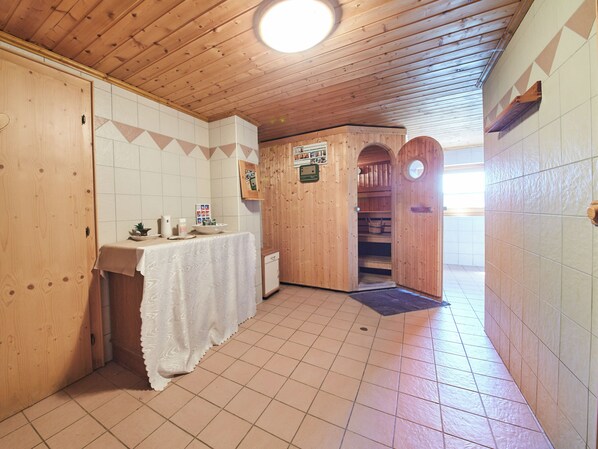 Un intérieur en bois avec un sol carrelé, une table recouverte d’une nappe blanche et un buffet en bois doté d’une porte.