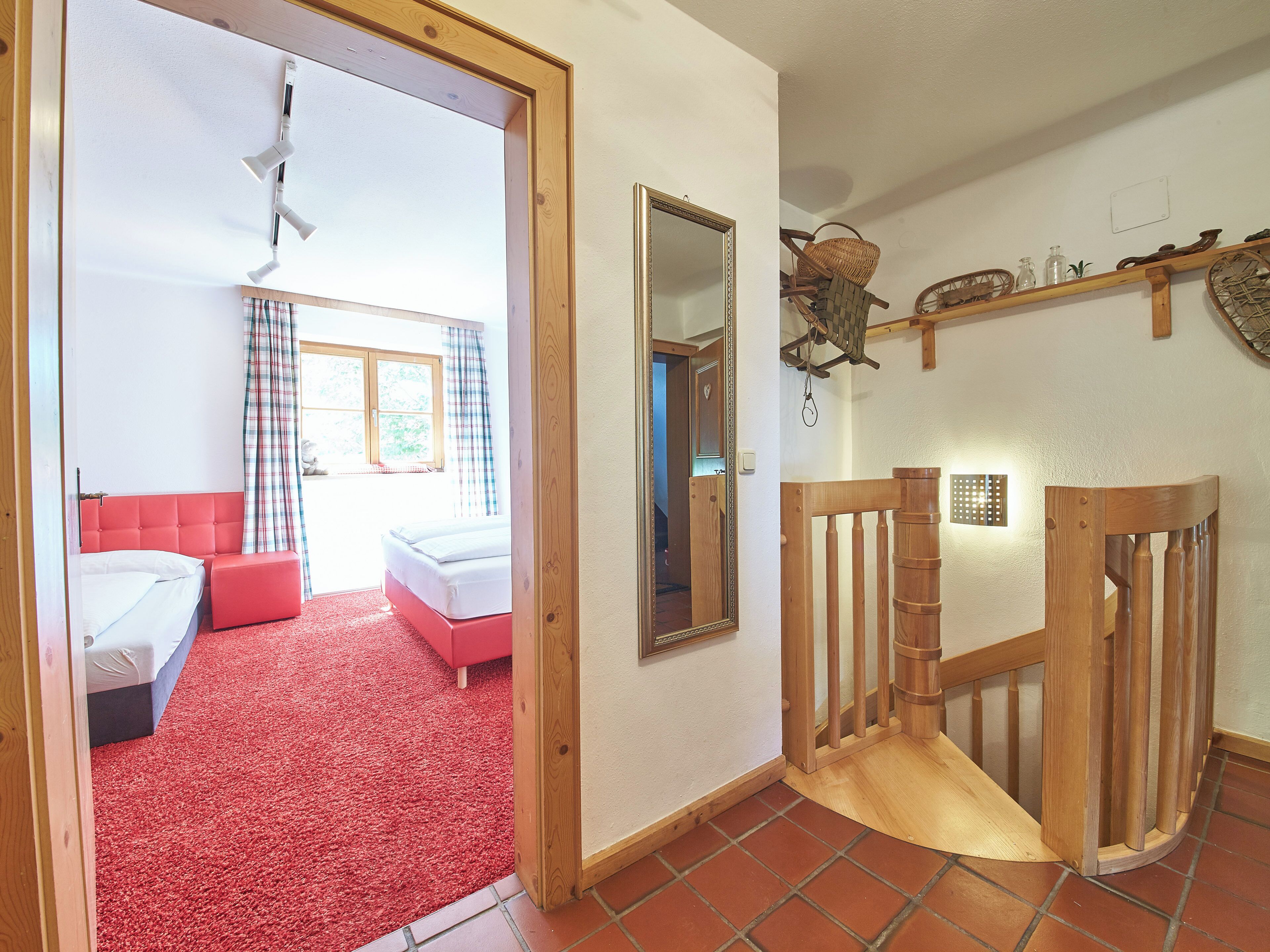 A room with a bed, a red chair, a wooden staircase, and a mirror on the wall.