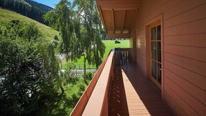 A wooden balcony with a view of a green hillside and a distant building. - Chalet Felix by we rent (Saalbach)