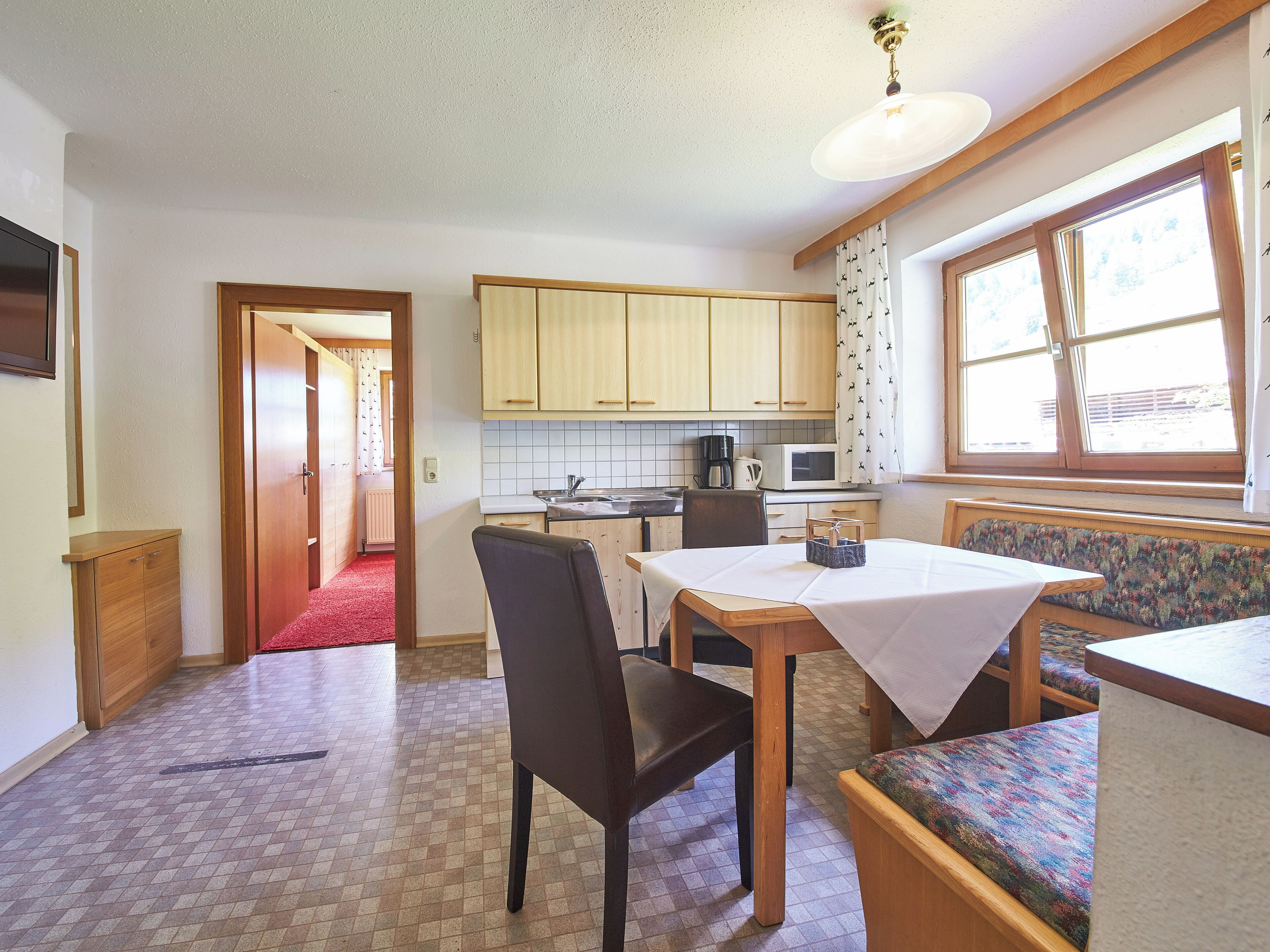 Une cuisine compacte avec des meubles en bois, une table à manger avec des chaises, un four à micro-ondes et une fenêtre avec des rideaux.