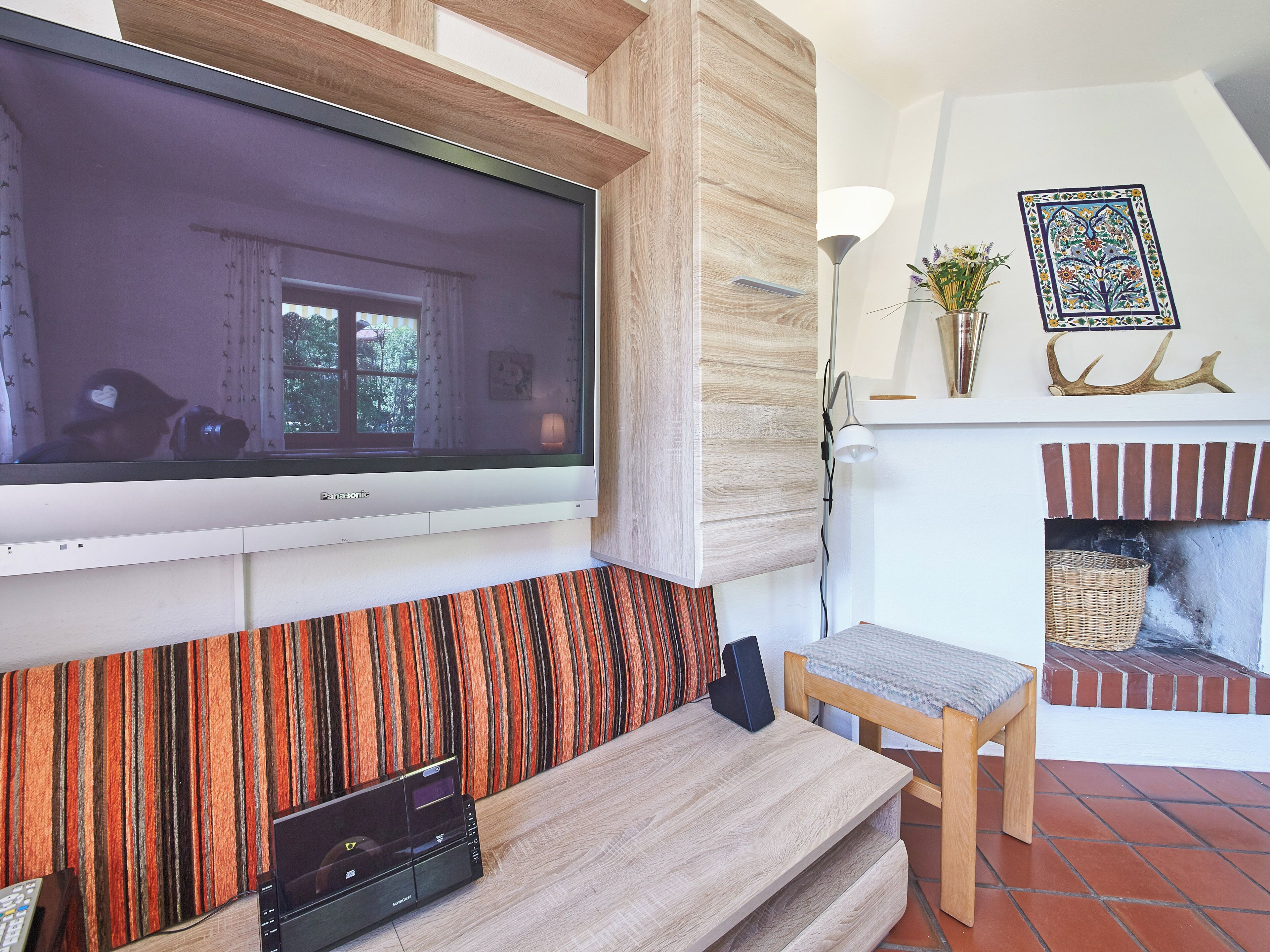 Una sala de estar con televisión de pantalla plana montada en la pared, un banco de madera, chimenea y un papel tapiz estampado.
