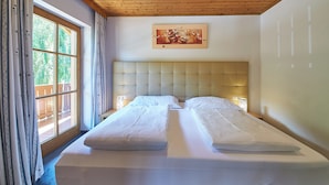 A double bed with a tufted headboard in a room with wooden ceiling and large windows. - Chalet Felix by we rent (Saalbach)