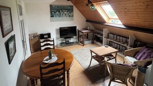 Un acogedor cuarto en el ático con techo de madera, una mesa de comedor con sillas, un televisor y una estantería.