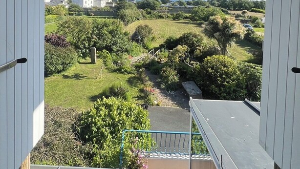 Un balcón con vistas a un jardín ajardinado y edificios a la distancia.