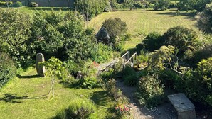 Un exuberante jardín con diversas plantas y árboles, un banco de piedra y un pequeño estanque.