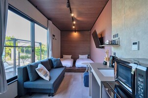 A modern hotel room with a sofa, two beds, a TV, and a kitchenette.