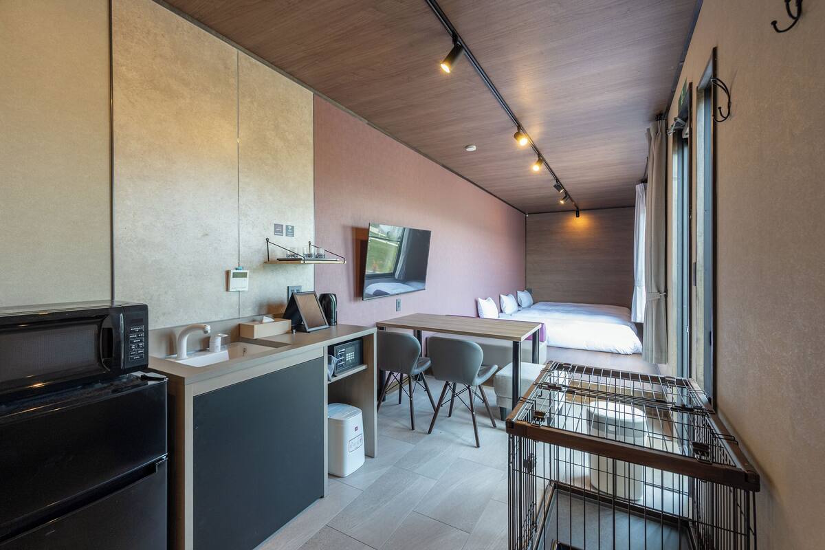 Habitación de hotel pequeña con kitchenette, cama, televisor y vistas al exterior.