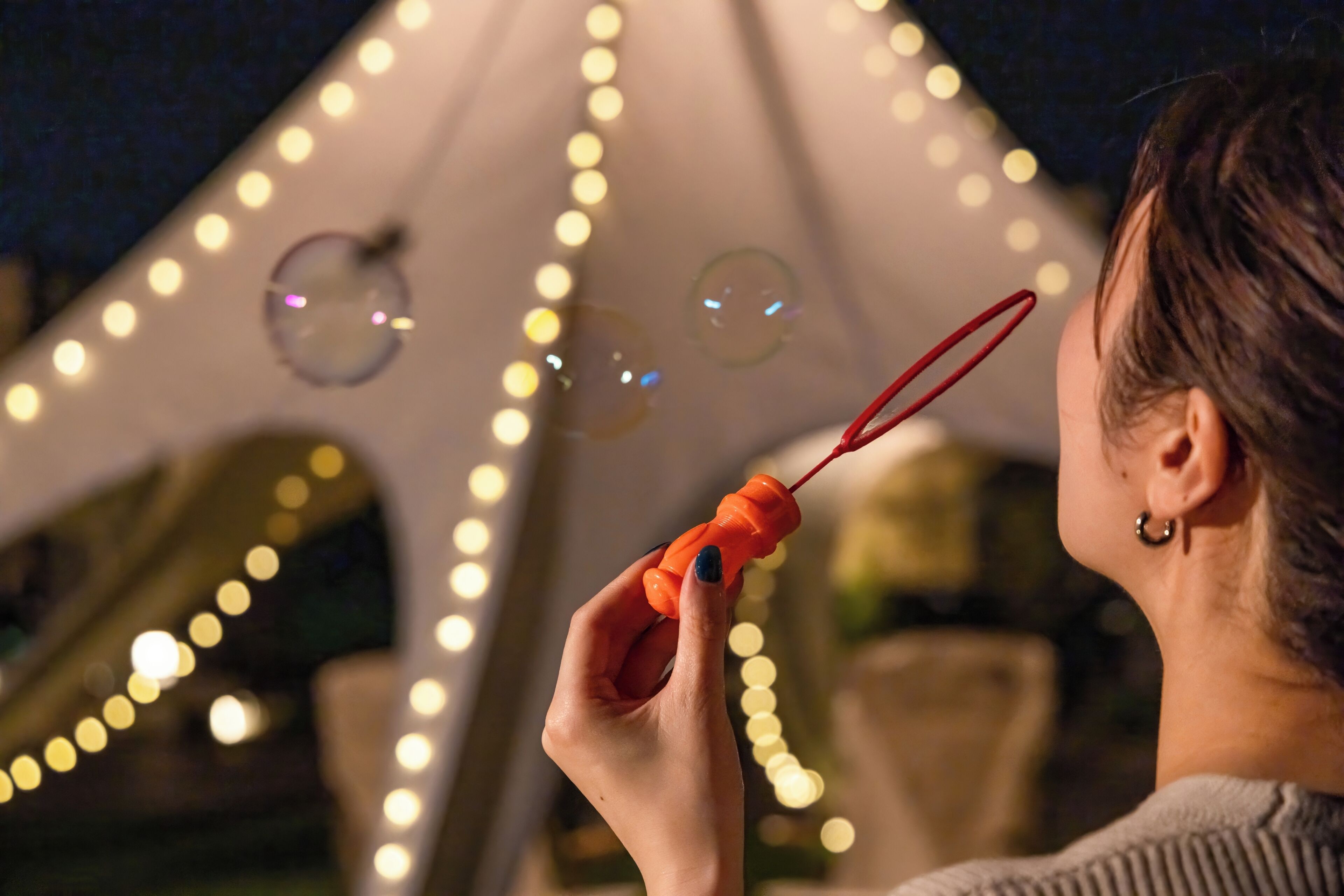 A person blowing bubbles with a bubble wand outdoors at night.