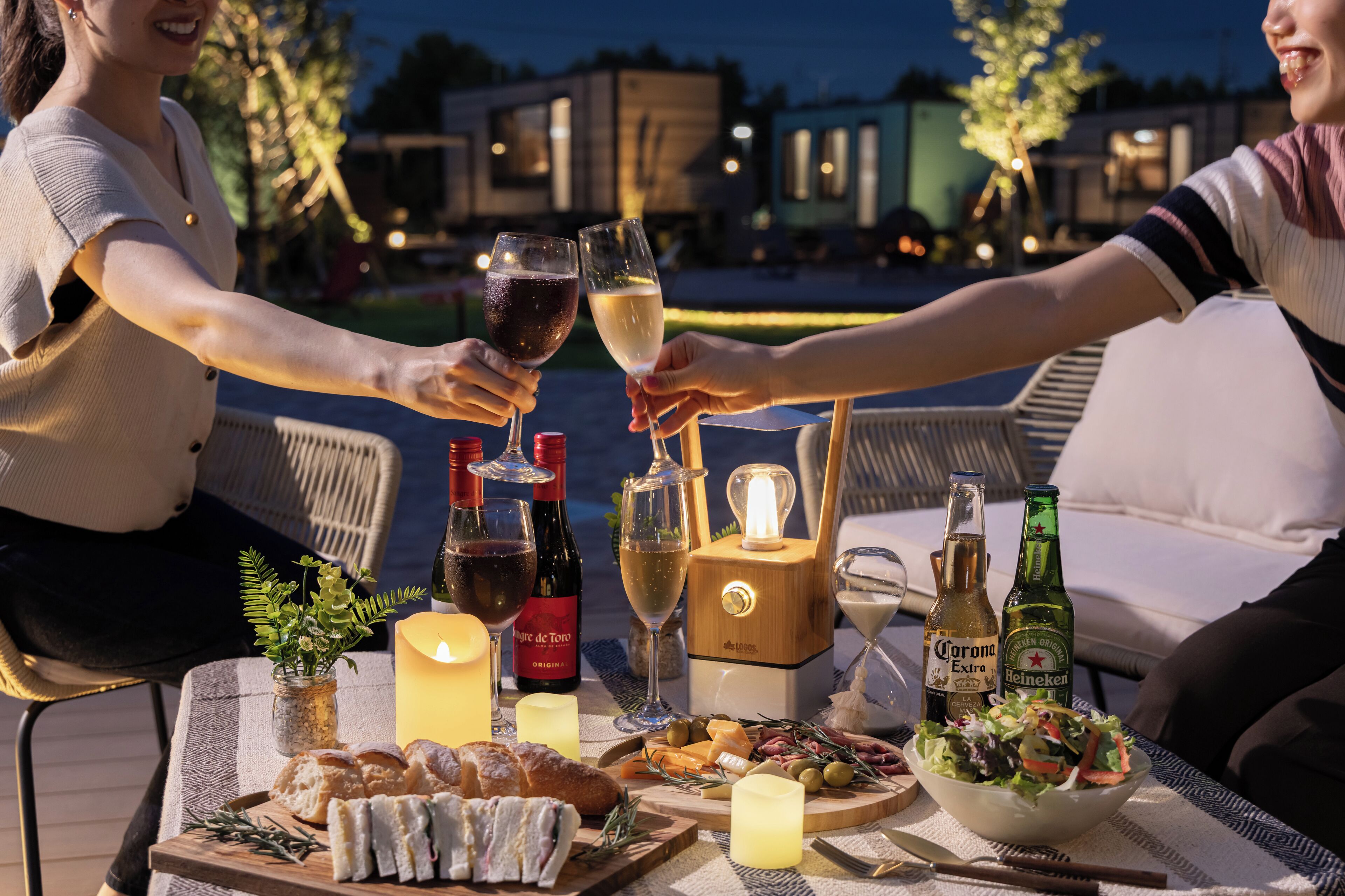 An outdoor dining setup with a table, candles, bottles of wine, and a variety of food.