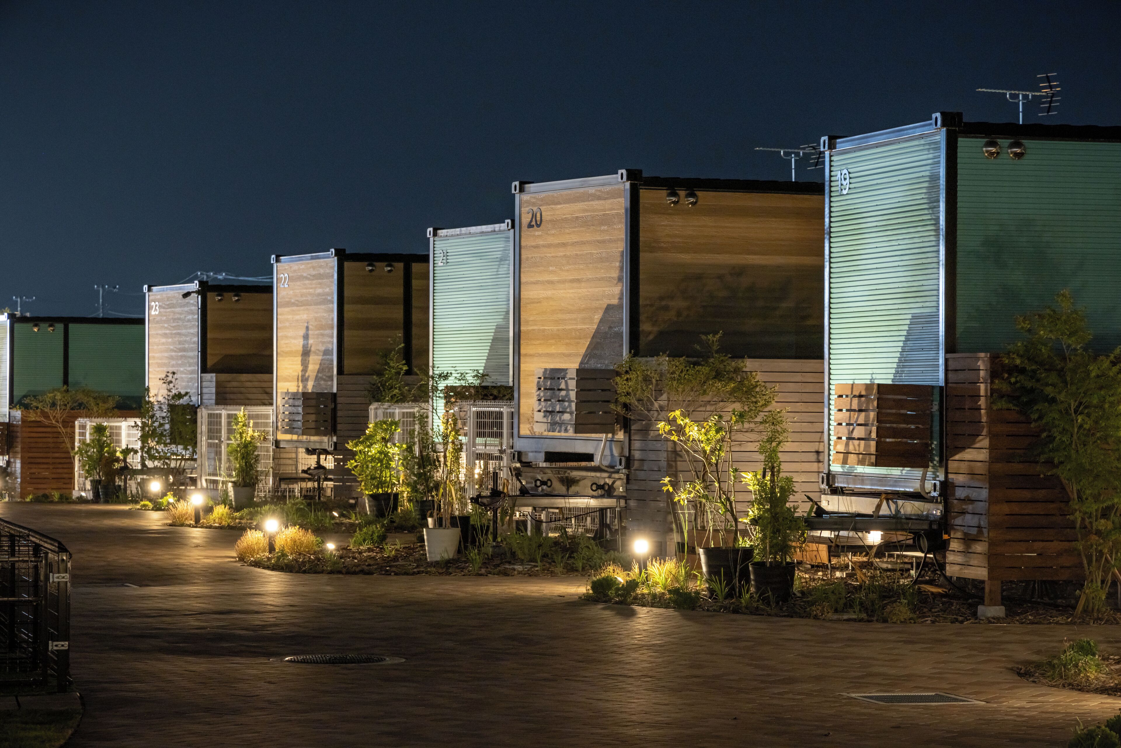 A row of modular cabins with numbered doors, a paved driveway, and outdoor lighting.